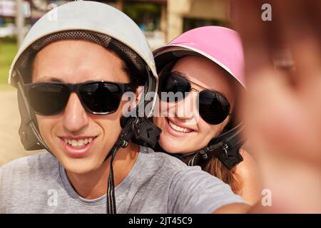 Roadtrip-Erinnerungen. Ein junges Paar, das zusammen ein Selfie gemacht hat, während es auf einem Roller unterwegs ist. Stockfoto