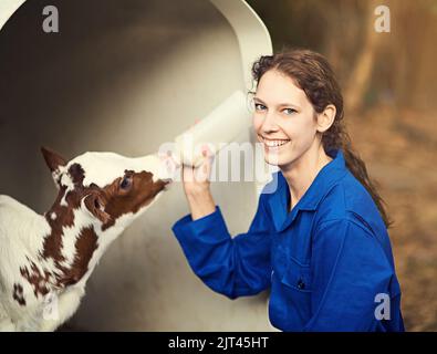 Vieh ist meine Leidenschaft. Porträt einer Bäuerin, die auf dem Bauernhof ein Kalb von Hand füttert. Stockfoto