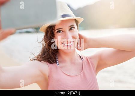 Selfies am Meer. Eine glückliche junge Frau, die mit ihrem Telefon ein Selfie an einem tropischen Strand macht. Stockfoto