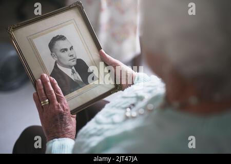 Er war so ein netter und fürsorglicher Mann... eine ältere Frau, die ein altes Schwarz-Weiß-Foto eines Mannes ansah. Stockfoto