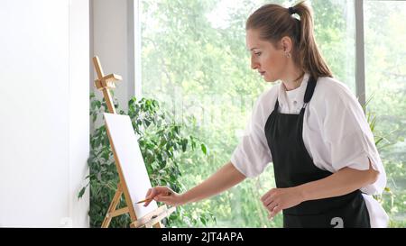 Reife Dame Schublade schafft Meisterwerk gegen große Fenster Stockfoto