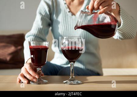 Gießen Sie frischen hausgemachten Rote-Beete-Saft aus einer Kanne in zwei Gläser. Gesunde Ernährung. Stockfoto