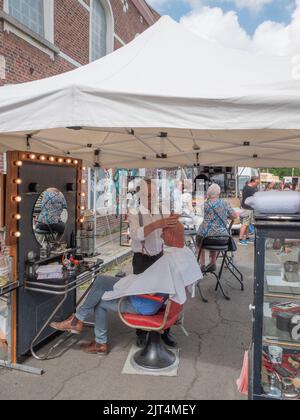 Sint Gillis Waas, Belgien, 21. August 2022, rasiert ein älterer Barbier während einer Straßenmesse den Kopf eines Mannes Stockfoto