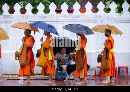 Vientiane, Laos. 26. August 2022. Eine Frau bietet buddhistischen Mönchen in Luang Prabang, Laos, Almosen an, 26. August 2022. Die Provinz Luang Prabang, etwa 220 km nördlich der laotischen Hauptstadt Vientiane, ist eine der bekanntesten Provinzen in Laos und wegen ihrer alten Tempel, landschaftlichen Attraktionen und ländlichen Landschaften eine der beliebtesten Touristenattraktionen. Wissenschaftliche und kulturelle Organisation (UNESCO) als Weltkulturerbe im Jahr 1995. Kredit: Kaikeo Saiyasane/Xinhua/Alamy Live Nachrichten Stockfoto