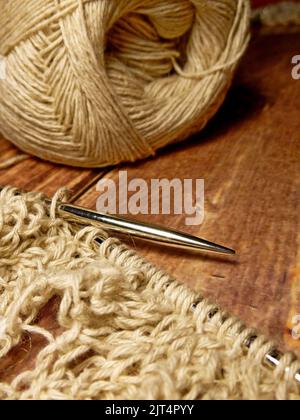 Durchbrochene Tischdecke beim Stricken. Stricknadeln, Schlaufen auf Stricknadeln, Strickstoff, Fadenknäuel, grobe Baumwolle und Leinen Stockfoto