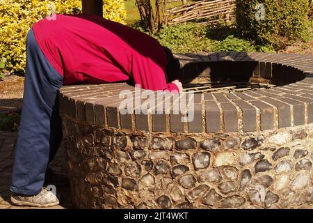 Ein Mann mit 60+, der im Garten des Brandon Country Park, Suffolk, England, einen gut gemachten mit Flintknapping mit grauen Ziegeln überblickt Stockfoto