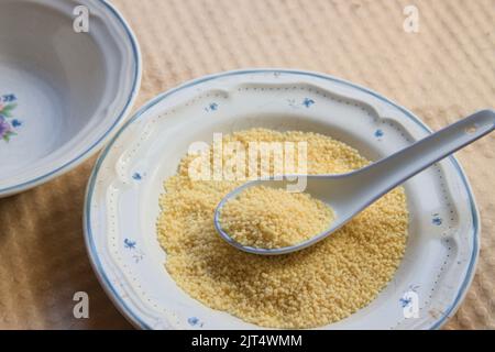 Bild eines Tellers, in dem sich etwas roher Grieß mit einem Porzellanlöffel auf einer Kartonoberfläche befindet Stockfoto