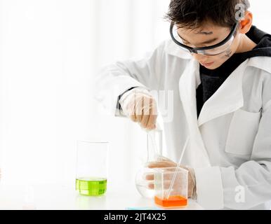 Schuljunge, der Chemie-Experiment macht, um chemische Flüssigkeiten in der Grundschule zu messen. Clevere Pupille, die die Testergebnisse im Labor analysiert Stockfoto