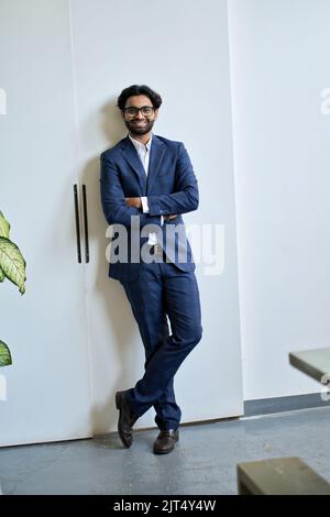Glücklicher junger indischer Geschäftsmann trägt Anzug steht im Büro, vertikales Porträt. Stockfoto