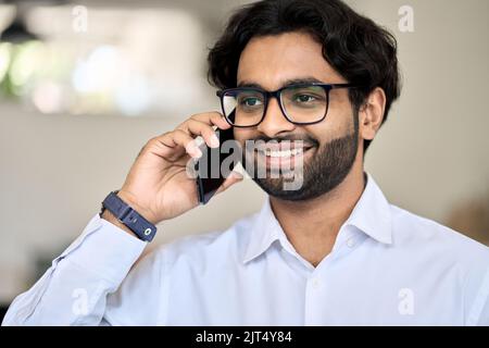 Lächelnder junger indischer Geschäftsmann, der am Telefon telefoniert. Stockfoto