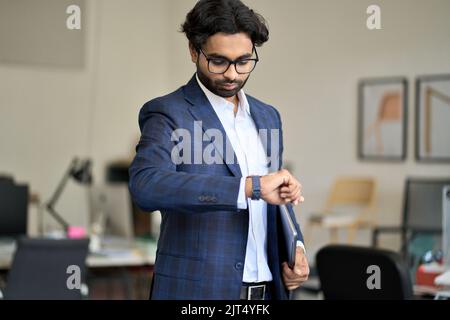 Ein geschäftiger indischer Geschäftsmann, der die Zeit überprüft und im Büro die Uhr anschaut. Stockfoto