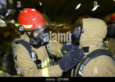 U.S. Navy Aircrew Survival Equipmentman 3. Class Left, hilft, Controlman Fireman mit seiner Schutzausrüstung während einer allgemeinen Quarterübung in der Hangarbucht des Flugzeugs 140117 zu beschädigen Stockfoto