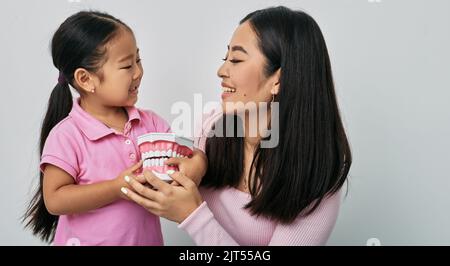 Pflege der Kinderzähne. Asiatische Mutter lehrt ihre kleine Tochter über Zahnhygiene und wie man richtig für ihre Zähne mit pädagogischen j zu pflegen Stockfoto