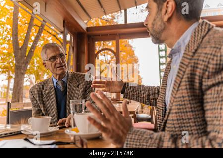 Zwei ältere Geschäftsleute unterhalten sich im Café, während sie Kaffee trinken Stockfoto