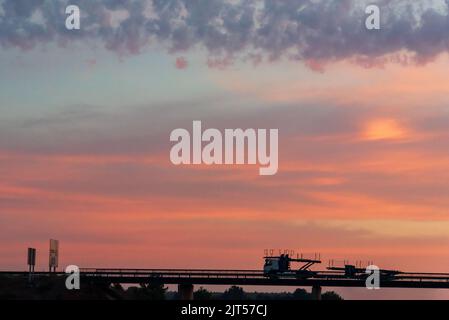 Autotransporter, der bei Sonnenaufgang auf einer Brücke zirkuliert. Stockfoto