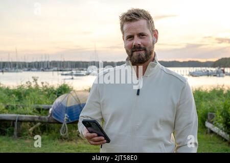 Glücklicher junger, gutaussehender kaukasischer Hipster-Mann, der im Park telefoniert Stockfoto
