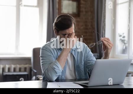 Müder, tausendjähriger Geschäftsmann sitzt am Laptop und reibt Augenlider Stockfoto