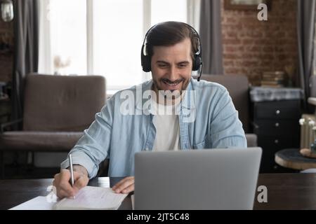 Glücklicher Mann mit einem Notebook der Generation Y, der ein schnurloses Headset trägt Stockfoto