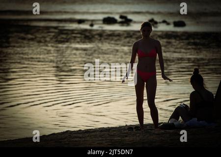 Warschau, Polen. 26. August 2022. Eine Frau im Bikini wird am 26. August 2022 an einem Strand im Zentrum von Warschau, Polen, gegen das von der Weichsel reflektierte Licht silhouettiert. Obwohl die Durchschnittstemperatur in Polen im August in den letzten Wochen etwas über 19 Grad Celsius beträgt, haben die Temperaturen täglich Höchststände von mehr als 30 Grad erreicht. (Foto von Jaap Arriens/Sipa USA) Quelle: SIPA USA/Alamy Live News Stockfoto