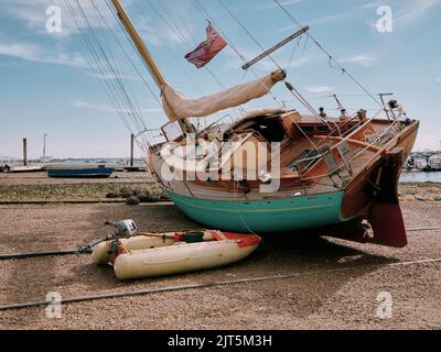 Eine Yacht auf der harten Sommerlandschaft bei Ebbe und Flut und Boote in West Mersea Harbour, Mersea Island, Essex England Stockfoto