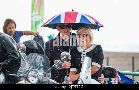 Brighton, Großbritannien. 28. August 2022. Dieses Paar steht unter einem Union Jack Regenschirm während einer Dusche, während Hunderte von Mods heute in Brighton sind, während sie ihre Mod Weekender Veranstaltung genießen, die eine Fahrt auf ihren Motorroller und verschiedene Live-Musik-Shows umfasst. : Credit Simon Dack/Alamy Live News Stockfoto