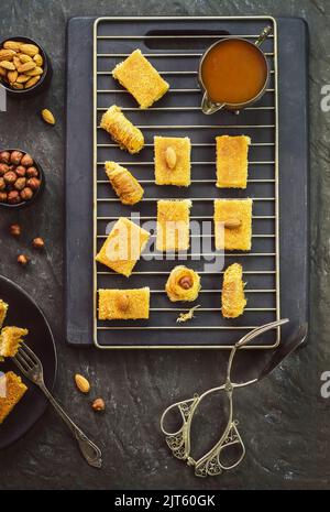 Arabische Küche; Sorten von nahöstlichen Gebäck und Ramadan Desserts Kunafa mit gerösteten Nüssen und Honig auf dunklem Hintergrund platziert. Stockfoto
