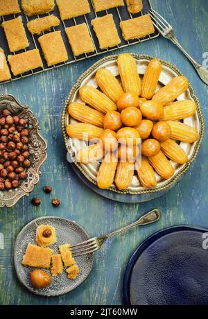 Verschiedene traditionelle Ramadan Desserts Kunafa, Luqaimat oder Luqmat al Kadi, Zeinab Finger und Nüsse auf blauem Hintergrund. Draufsicht mit Nahaufnahme. Stockfoto