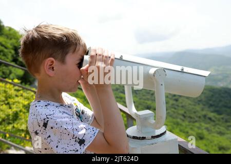 Der Junge blickt vom Una-koz-Grat, Adygea, durch ein Fernglas auf das Tal des Flusses Belaya Stockfoto