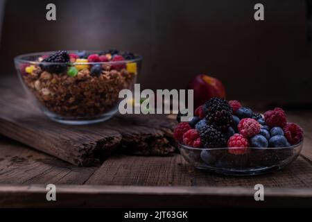 Beeren und Müsli in einer Glasschüssel. Bunte Beeren auf einem dunklen Baum. Stillleben der Beeren. Kochen Frühstück mit Beeren. Stockfoto