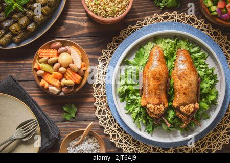 Arabische Küche, traditionelle ägyptische gefüllte Tauben oder Hamam Mahshi-Gericht. Serviert mit grünem Salat, orientalischen Gurken, Weinblättern und gekochtem Freekeh. Stockfoto