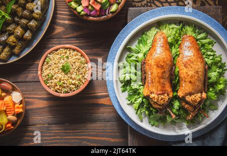 Arabische Küche, traditionelle ägyptische gefüllte Tauben oder Hamam Mahshi-Gericht. Serviert mit grünem Salat, orientalischen Gurken, Weinblättern und gekochtem Freekeh. Stockfoto