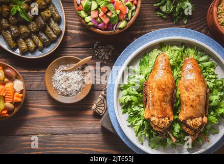 Arabische Küche, traditionelle ägyptische gefüllte Tauben oder Hamam Mahshi-Gericht. Serviert mit grünem Salat, orientalischen Gurken, Weinblättern und gekochtem Freekeh. Stockfoto