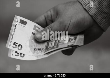 Eine Nahaufnahme in Graustufen mit Details auf einer Hand, die fünfzig Euro-Banknoten hält Stockfoto