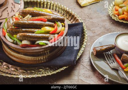 Arabische Küche; traditionelle ägyptische Wurst mit Zwiebeln, Paprika und Chilischoten. Serviert mit orientalischen Gurken, Tahini-Sauce und Pita-Brot. Stockfoto