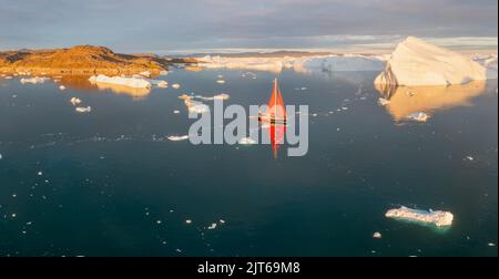 Ein kleines Schiff zwischen Eisbergen. Segelboot Kreuzfahrt unter schwimmende Eisberge in der Diskobucht Gletscher Mitternachtssonne Ilulissat, Grönland. Stockfoto