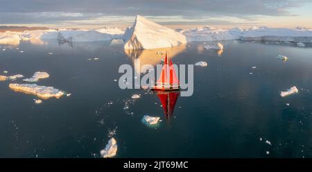 Ein kleines Schiff zwischen Eisbergen. Segelboot Kreuzfahrt unter schwimmende Eisberge in der Diskobucht Gletscher Mitternachtssonne Ilulissat, Grönland. Stockfoto