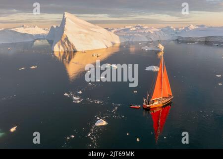 Ein kleines Schiff zwischen Eisbergen. Segelboot Kreuzfahrt unter schwimmende Eisberge in der Diskobucht Gletscher Mitternachtssonne Ilulissat, Grönland. Stockfoto