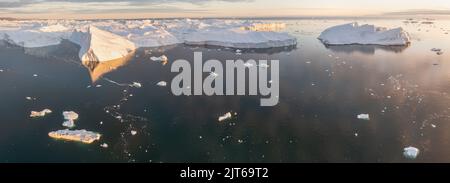 Ein kleines Schiff zwischen Eisbergen. Segelboot Kreuzfahrt unter schwimmende Eisberge in der Diskobucht Gletscher Mitternachtssonne Ilulissat, Grönland. Stockfoto