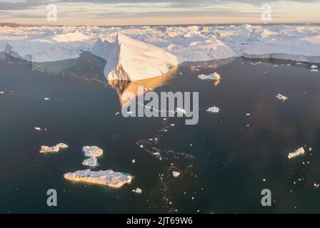 Ein kleines Schiff zwischen Eisbergen. Segelboot Kreuzfahrt unter schwimmende Eisberge in der Diskobucht Gletscher Mitternachtssonne Ilulissat, Grönland. Stockfoto