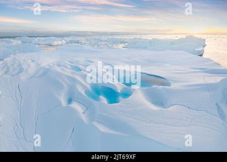 Arktische Naturlandschaft mit Eisbergen im grönländischen Eisfjord mit Mitternachtssonne. alpenglow am frühen Morgen während der Mitternachtssaison. Globale Erwärmung Stockfoto