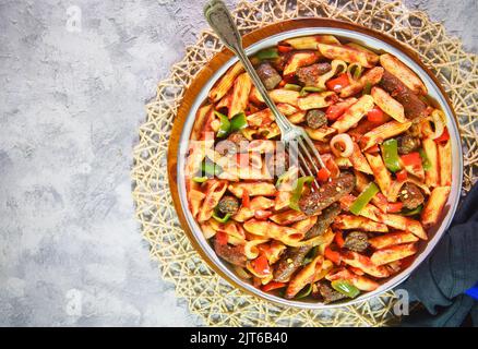 Arabische Küche; traditionelle ägyptische Pasta mit Wurst in einer weißen Pfanne auf rustikalem Hintergrund. Draufsicht mit Kopierbereich. Stockfoto