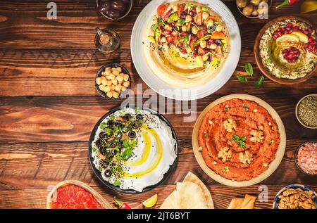 Arabische Küche: Sorten von köstlichen Meze und Dips aus dem Nahen Osten. Hummusplatte, Muhammara, Labneh, baba ghanough, Harissa und Oliven. Stockfoto