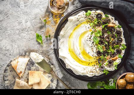 Arabische Küche: Nahöstlicher köstlicher Dip 'Labneh'. Frischkäse-Dip mit Olivenöl, Kräutern und Oliven serviert mit traditionellem Pita-Brot. Stockfoto
