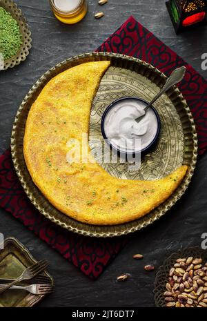 Arabische Küche: Traditionelles Backwaren aus dem Nahen Osten und das berühmte Dessert „Kunafa“ im Ramadan, serviert mit köstlicher Creme, Pistazien und Honigsirup. Stockfoto