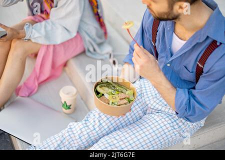 Stilvoller Mann und Frau essen gesunde Take-Away-Lebensmittel im Freien Stockfoto