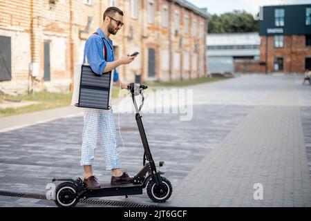 Stilvoller Kerl fährt Elektroroller und nutzt Handy unterwegs Stockfoto