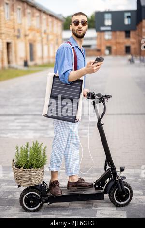 Stilvoller Kerl fährt Elektroroller und nutzt Handy unterwegs Stockfoto