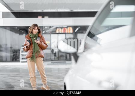 Porträt einer jungen Frau mit Telefon und Kaffee an der Tankstelle im Freien zu gehen Stockfoto