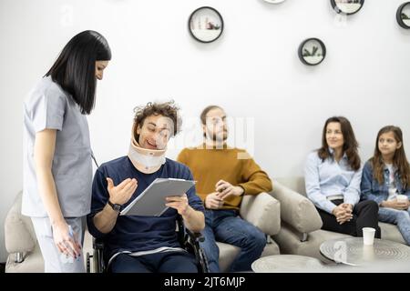Der Arzt kommuniziert mit dem Rollstuhlfahrer an der Klinikrezeption Stockfoto