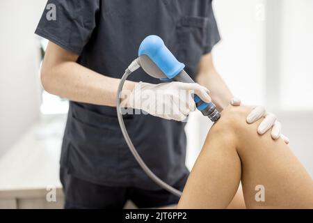 Der Arzt wendet eine Schockwellentherapie auf das Knie der Frau an Stockfoto